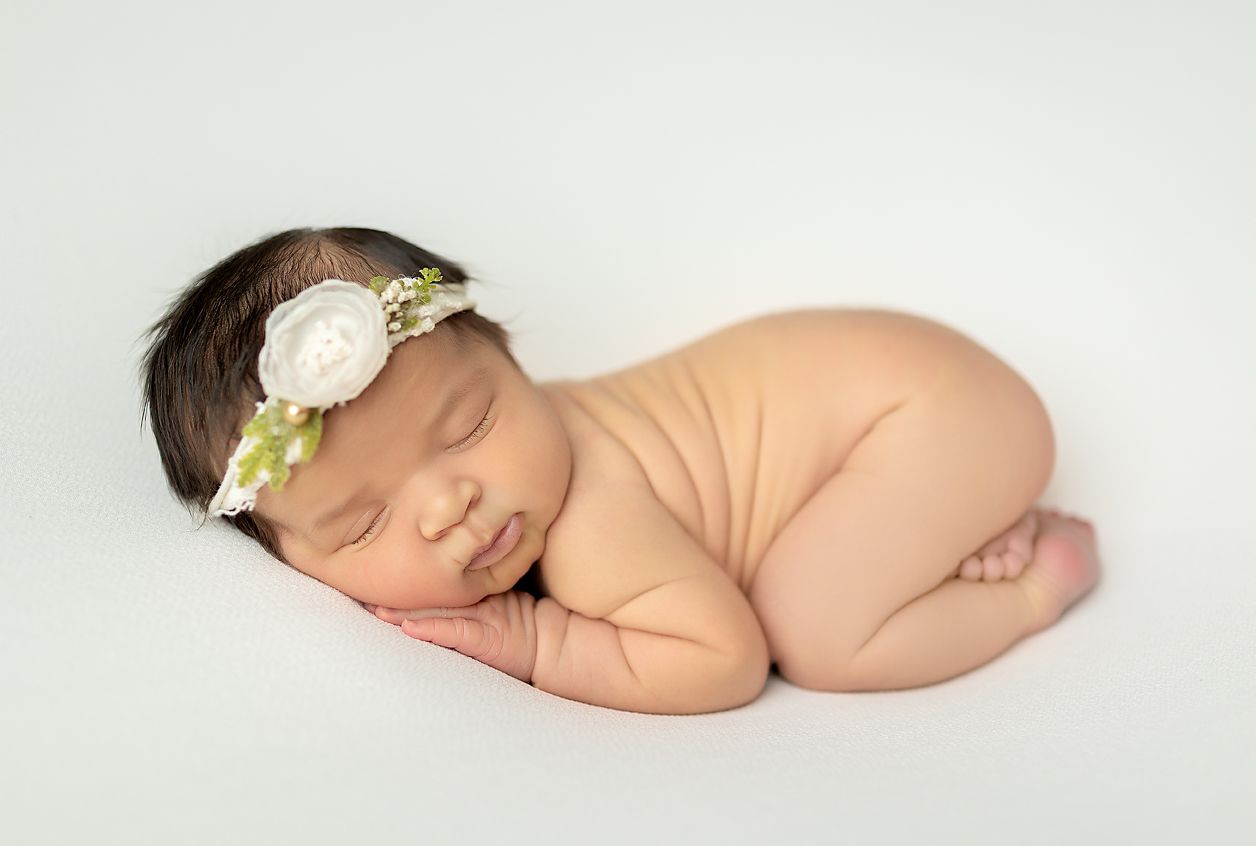 Newborn sleeping on a white blanket, wearing a floral headband.