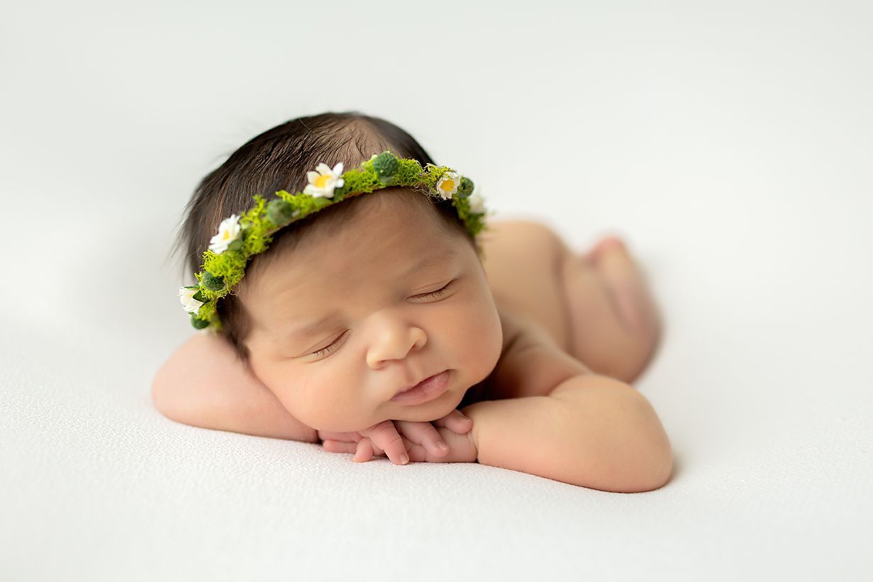 Newborn baby wearing a flower crown, sleeping on a white surface.