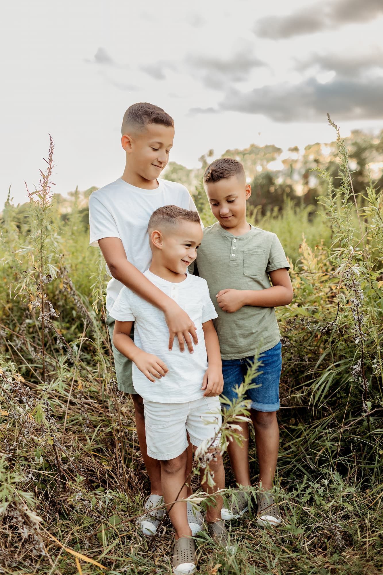 Three boys in casual clothes smile in a field of tall grass.
