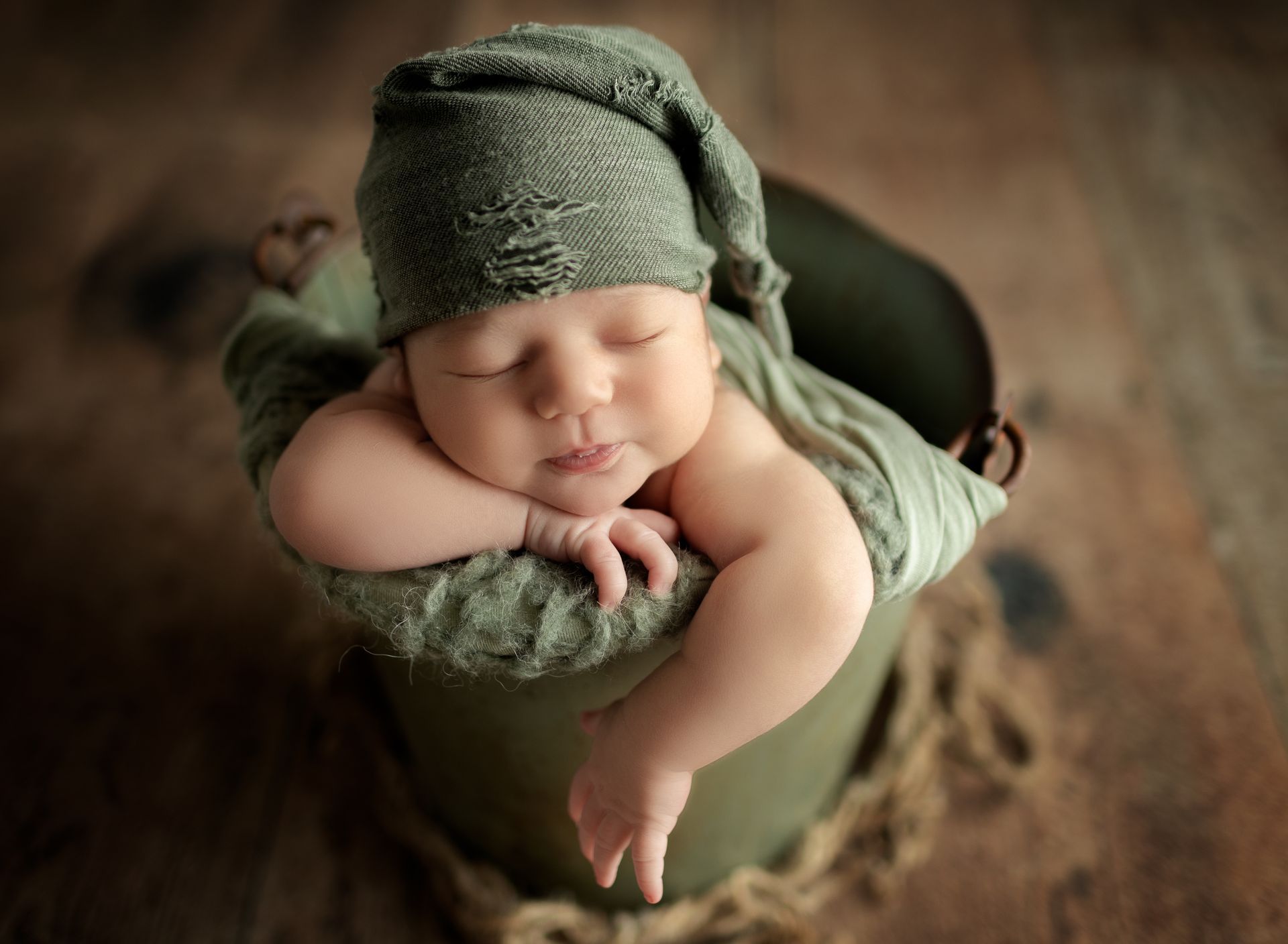 A newborn baby is sleeping in a green bucket.