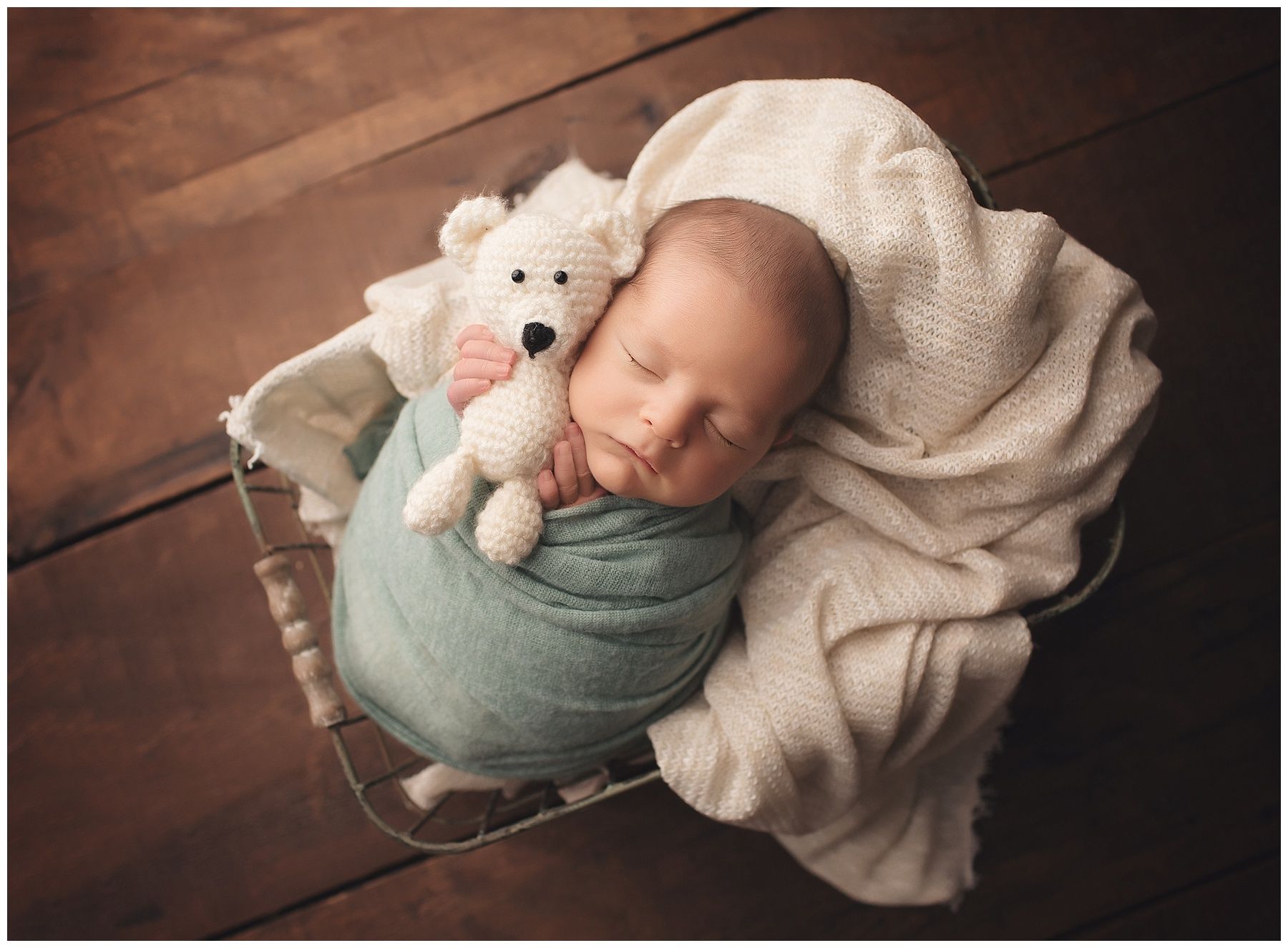 A newborn baby is sleeping in a basket with a teddy bear.