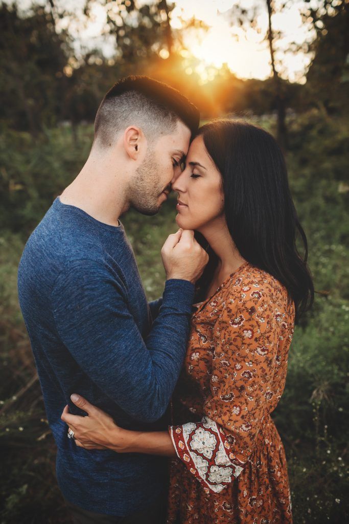 A man and a woman are touching their foreheads in a field at sunset.