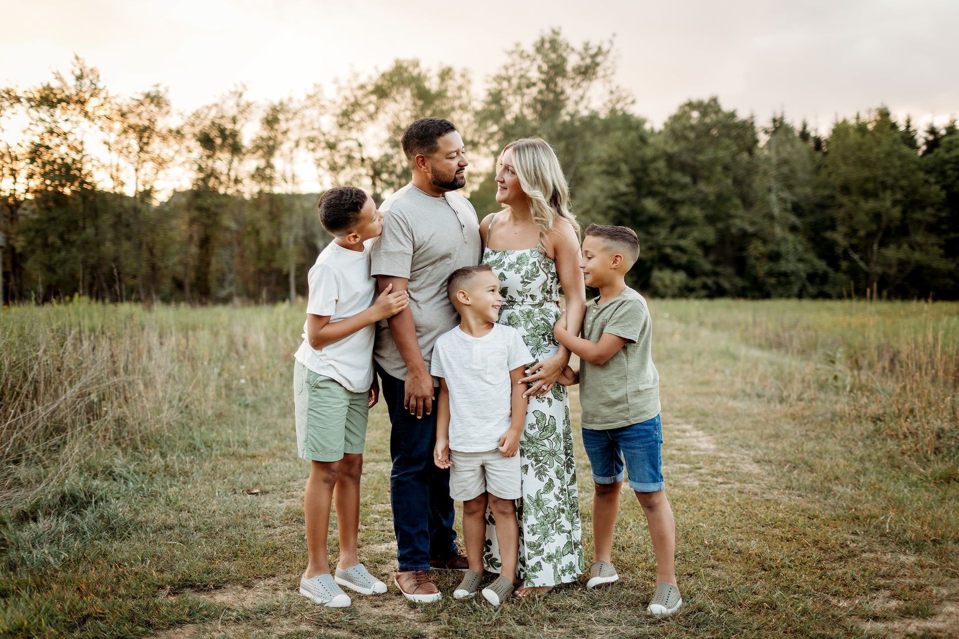 Family of five standing in a field, looking at each other. Sunset in background in Bergen County, NJ