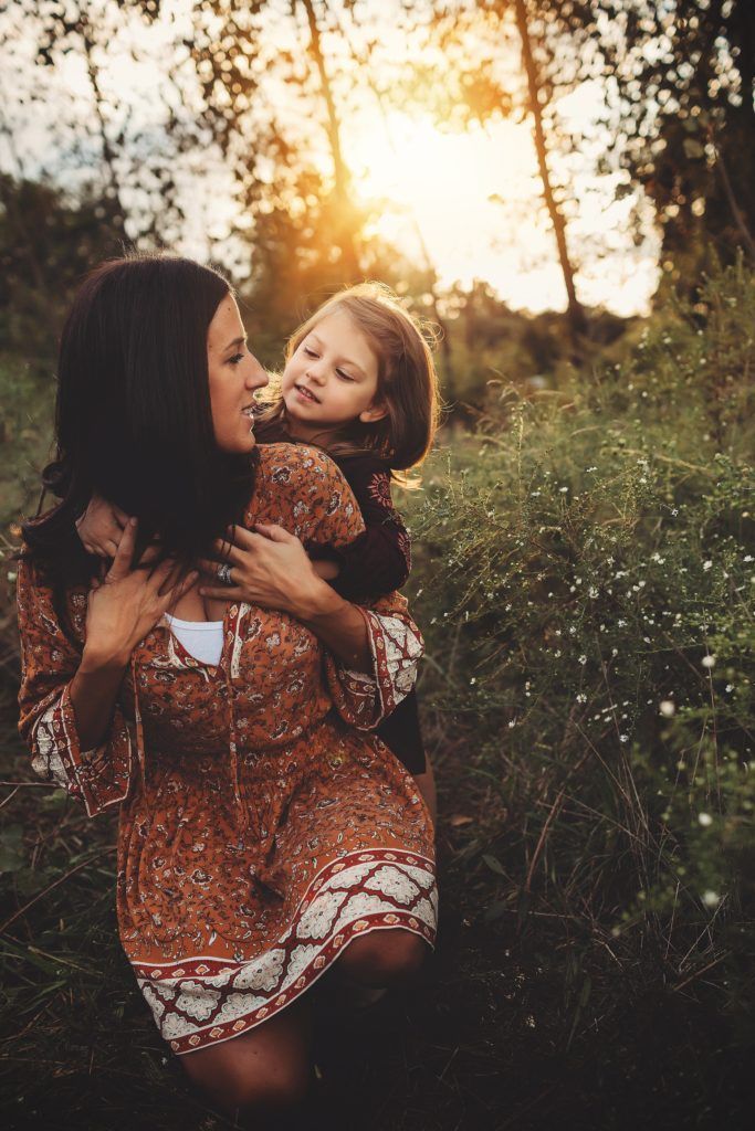 A woman is holding a little girl on her shoulders in a field.