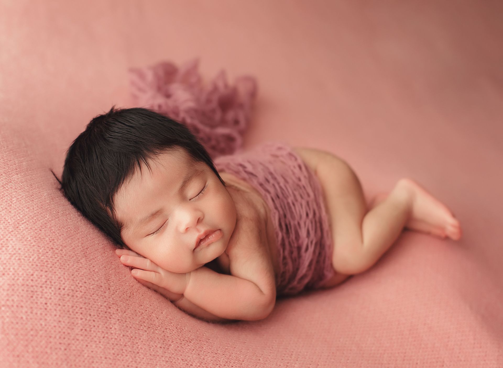 A newborn baby is sleeping on a pink blanket.