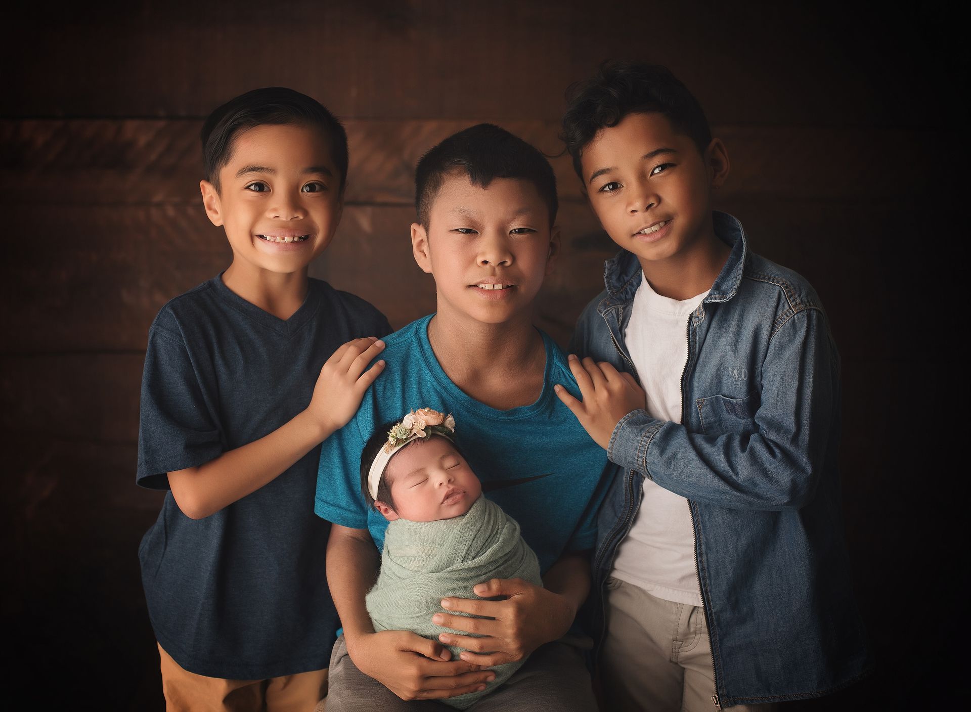Three boys are holding a newborn baby in their arms.