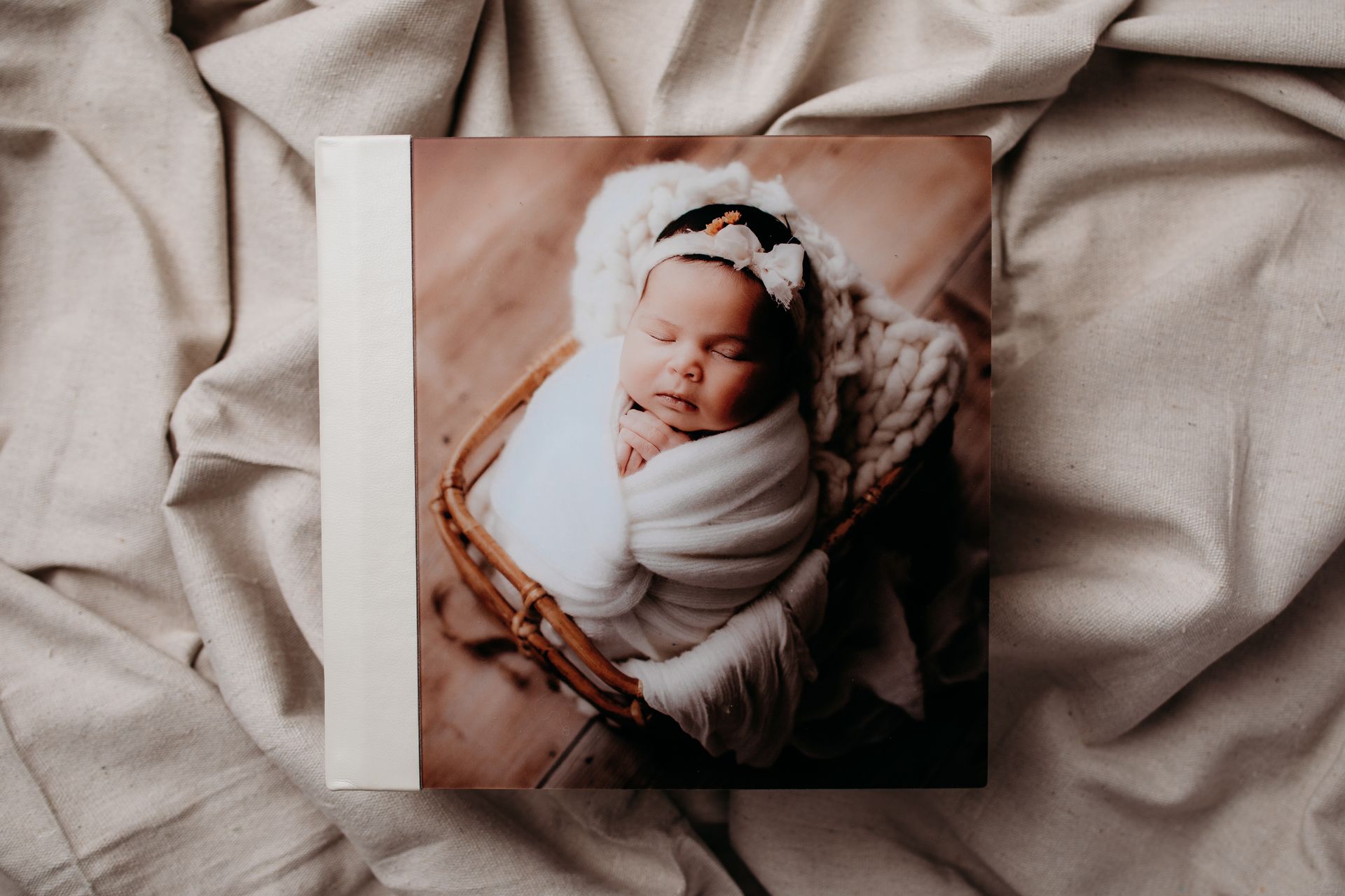 A baby is wrapped in a white blanket and sleeping in a basket.