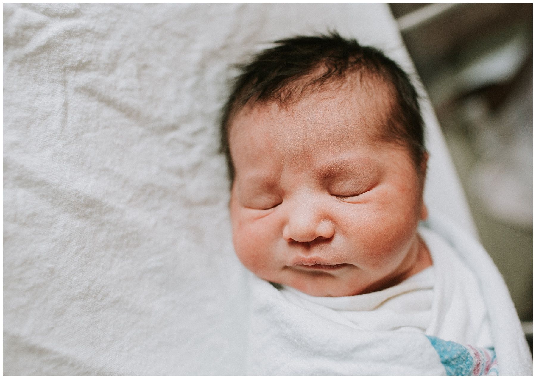 A newborn baby wrapped in a white blanket is sleeping in a hospital bed.