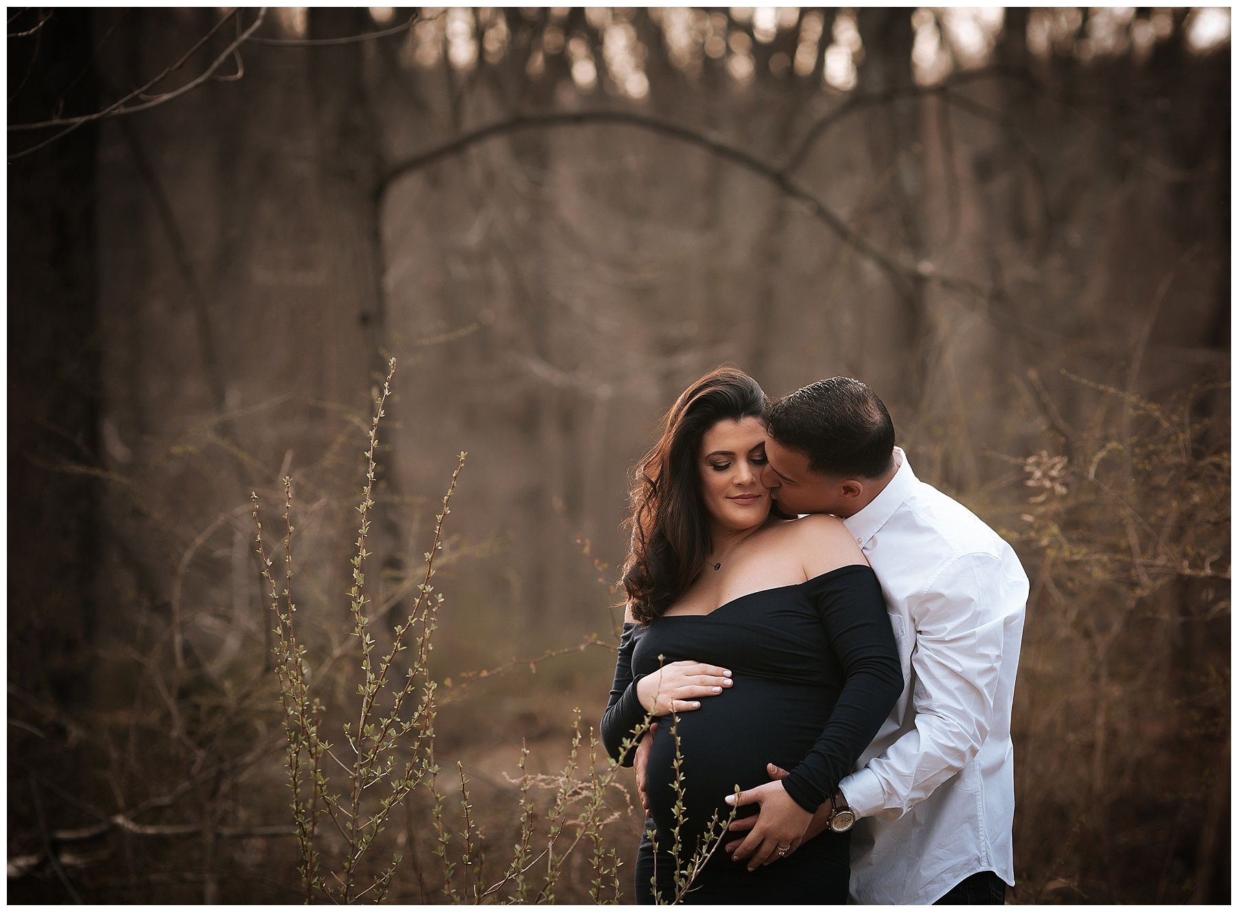 A man is kissing a pregnant woman on the cheek in a field.