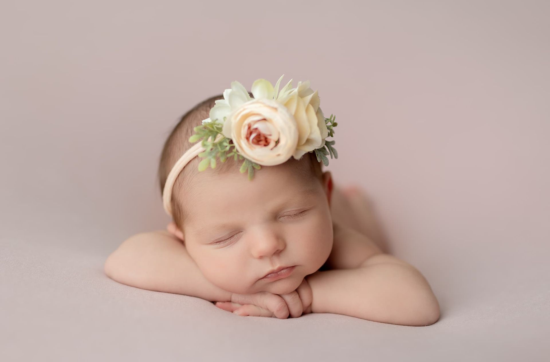 Newborn baby sleeping, curled on a white surface, wearing a white diaper wrap.