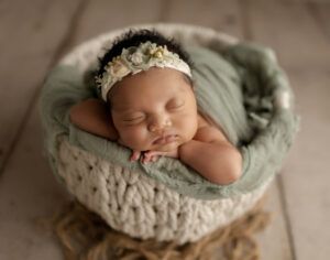A newborn baby is sleeping in a basket on a wooden floor.
