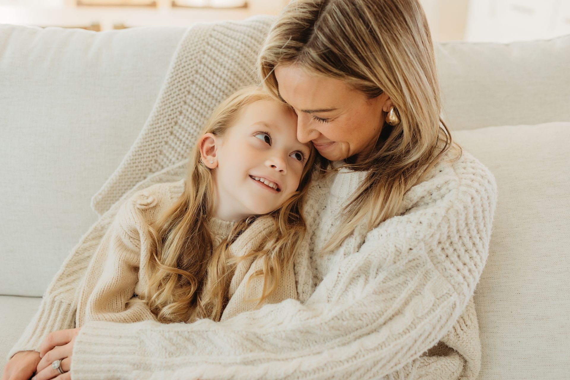 A woman and a little girl are sitting on a couch hugging each other.