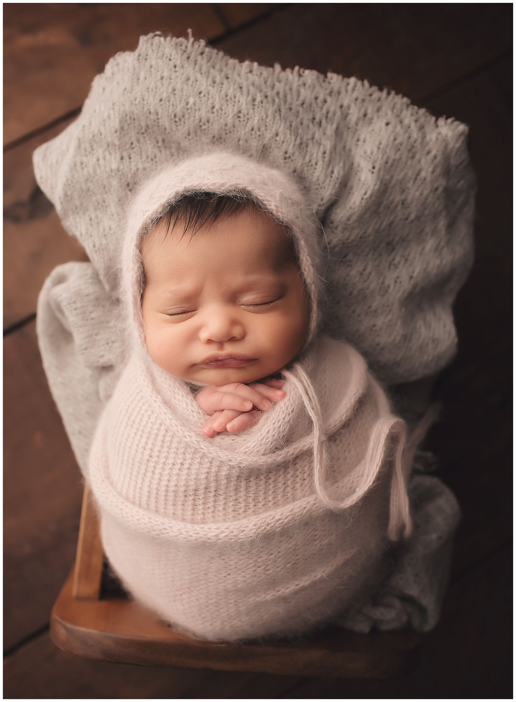 A newborn baby wrapped in a white blanket is sleeping in a chair.