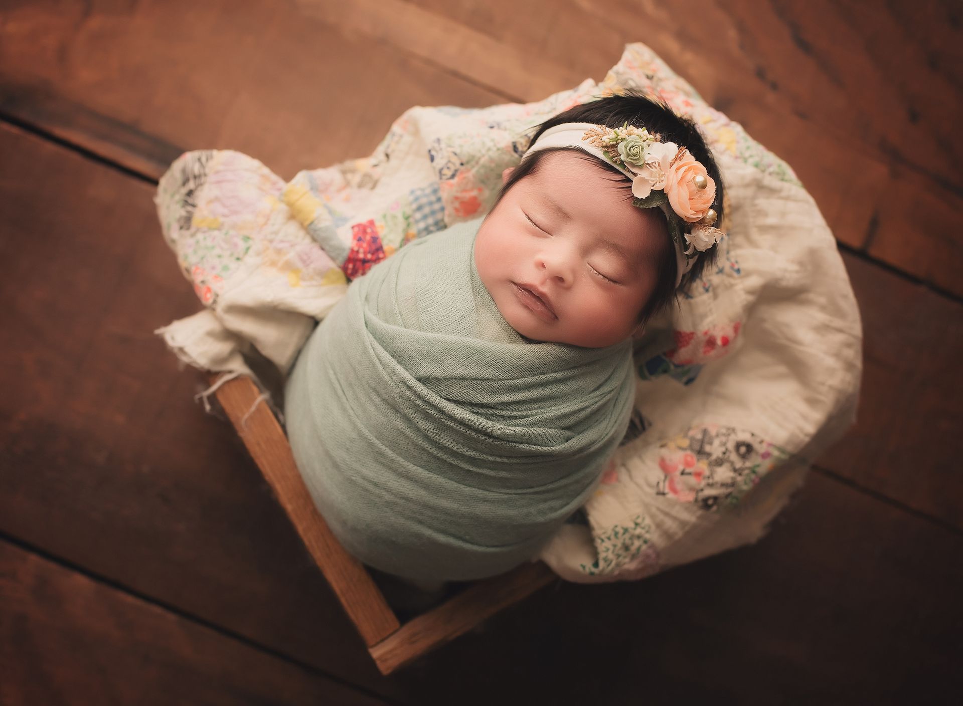 A newborn baby is wrapped in a blanket and wearing a flower headband.