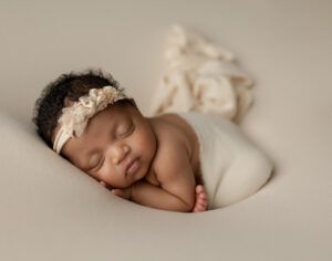 A newborn baby is wrapped in a white blanket and wearing a headband.