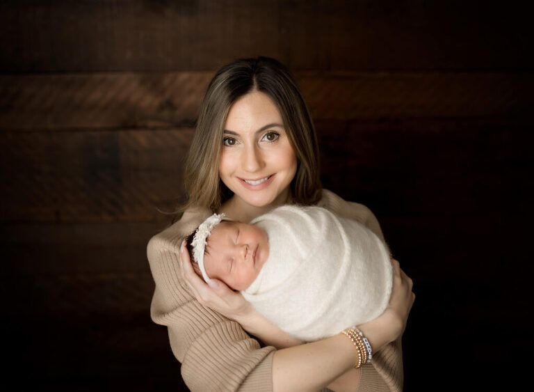 A woman is holding a newborn baby wrapped in a white blanket.
