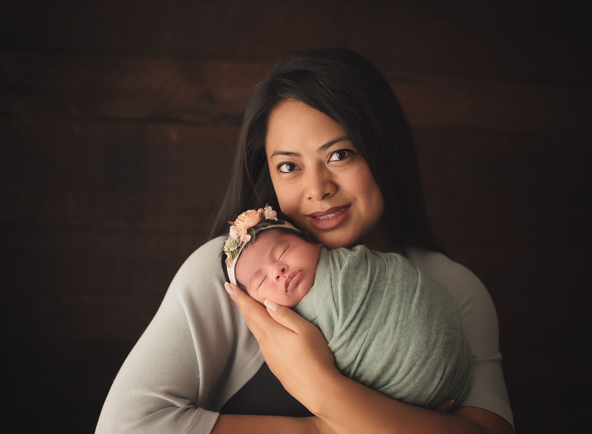 A woman is holding a newborn baby wrapped in a green blanket.