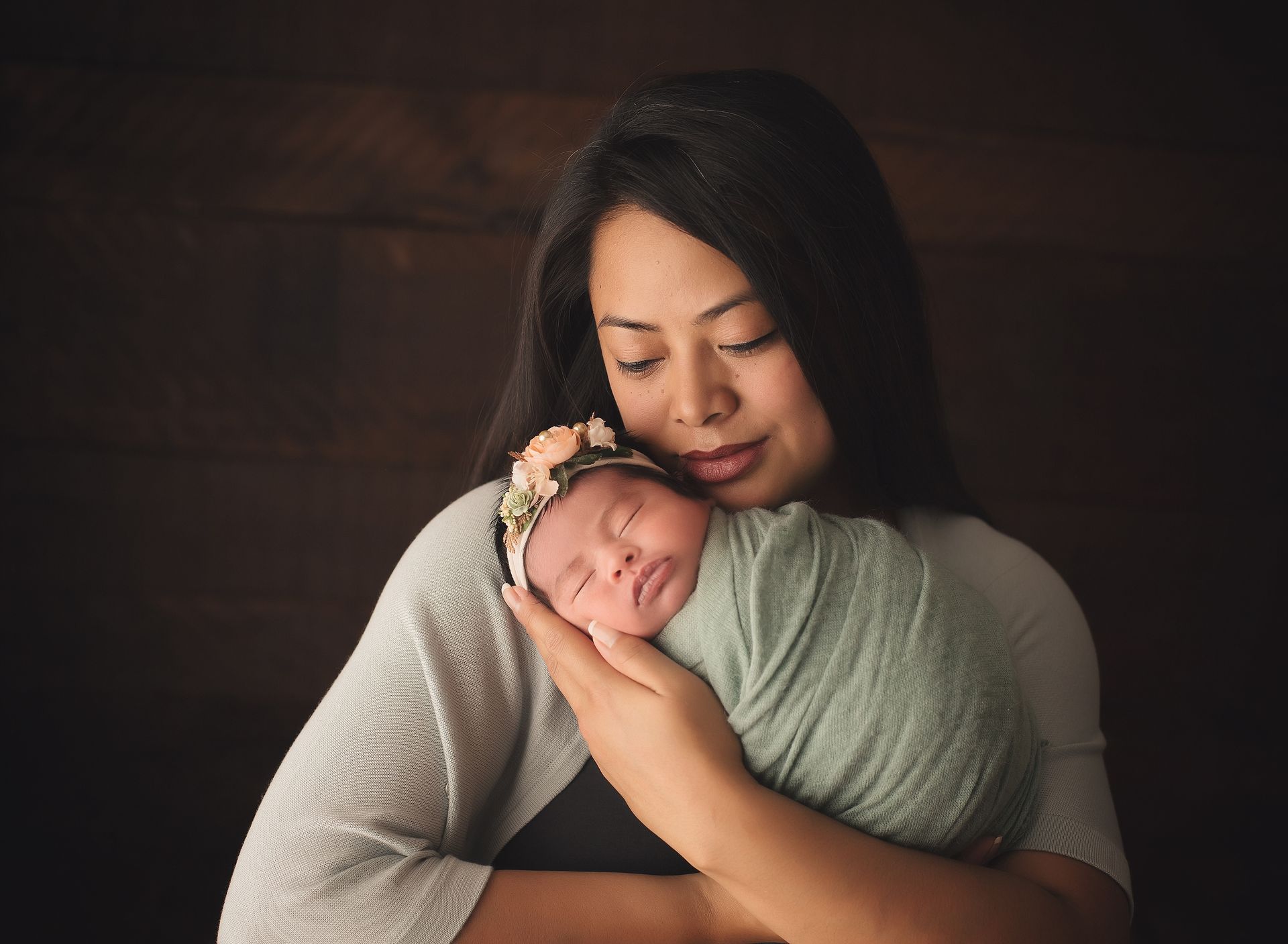 A woman is holding a newborn baby wrapped in a green blanket.