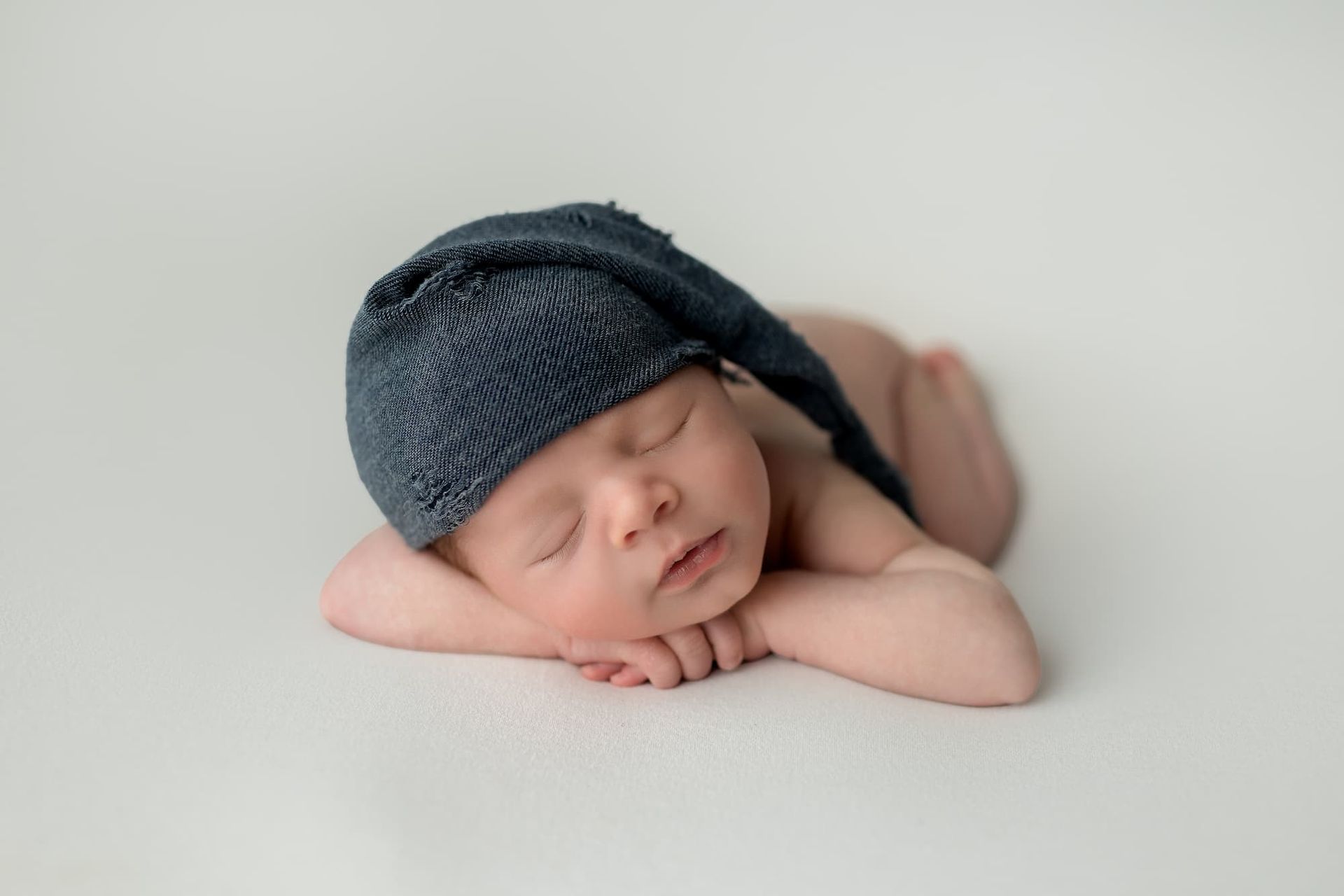 Newborn baby, wearing a blue knit cap, asleep, hands under chin, white background at a photoshoot in Begen County, NJ.