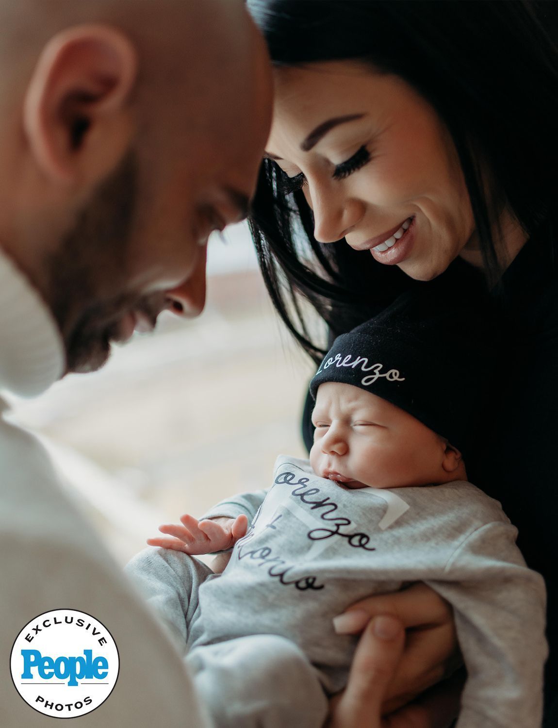 Parents gaze at their newborn baby wearing a hat and onesie in a hospital.