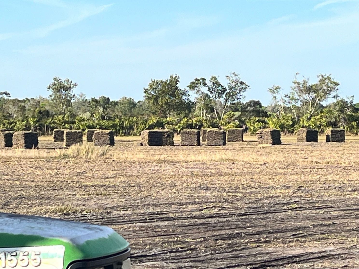A green tractor is parked in a field of hay bales.
