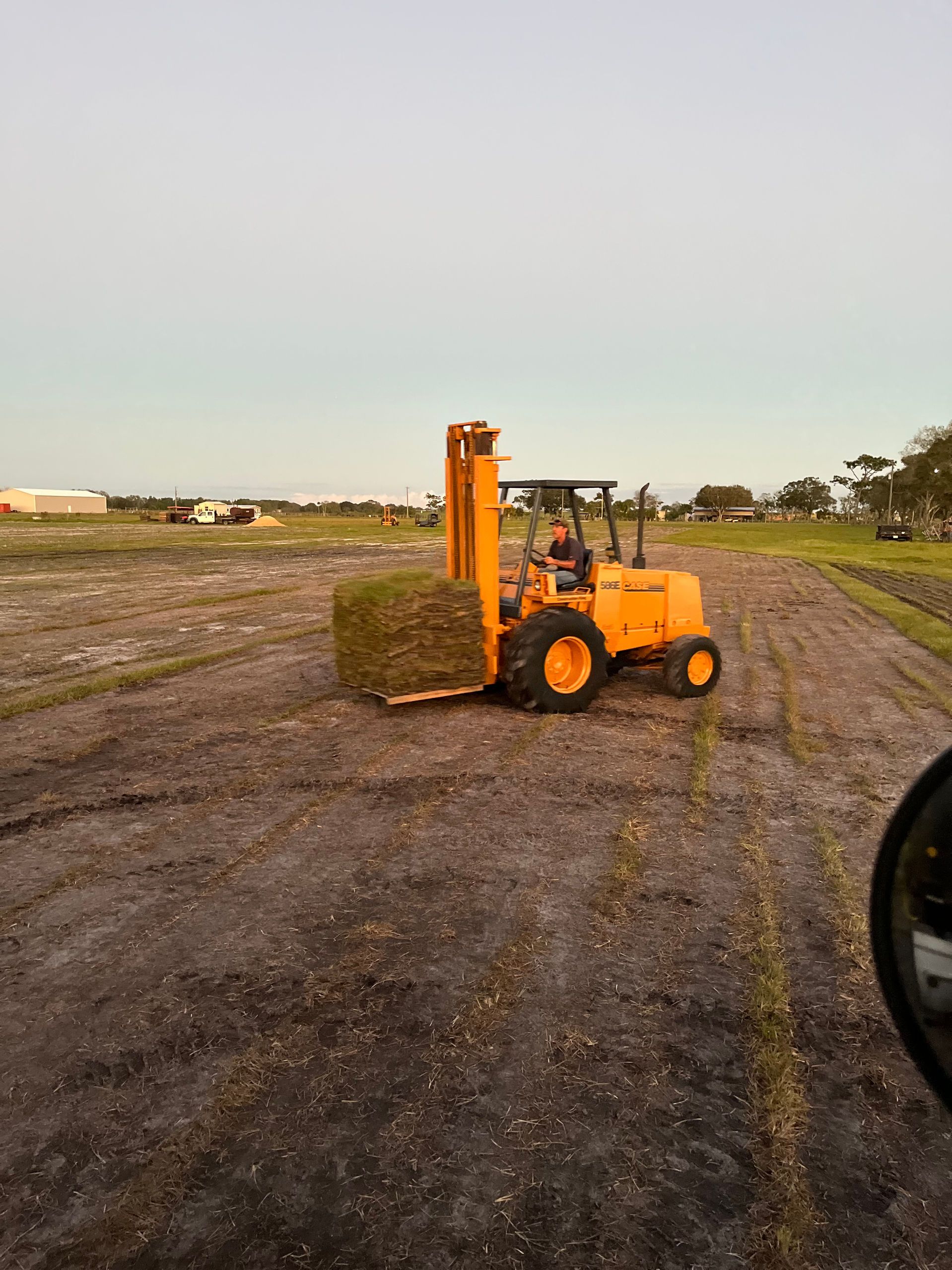 A yellow forklift is carrying a bale of hay in a field