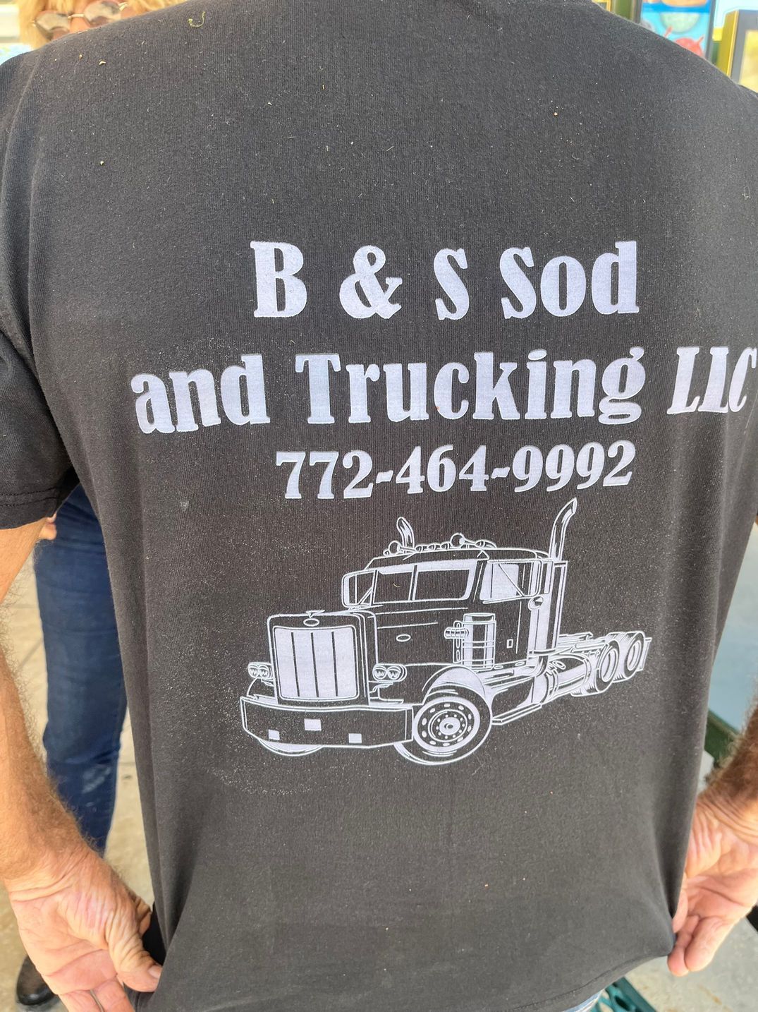 A man is wearing a t-shirt that says b & s sod and trucking llc