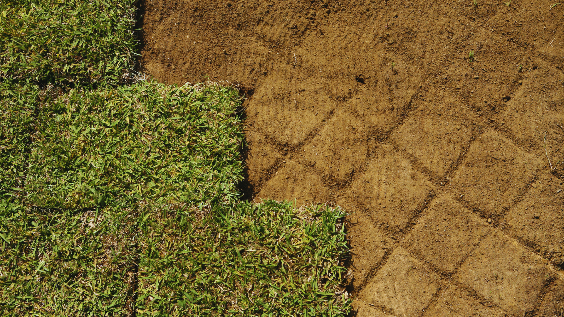 A man is rolling a roll of grass on the ground.