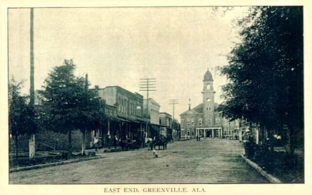 Street view of East End, Greenville, Alabama, with buildings, trees, and a clock tower in the background.