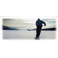 Person skating on ice, playing hockey with a stick, mountains in the background.