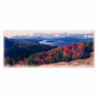 Panoramic view of a mountain landscape with a lake in the distance and trees with vibrant red foliage.