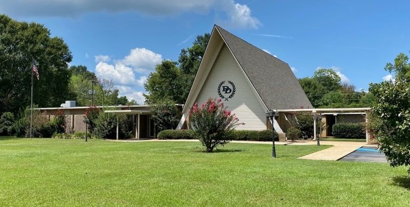 A-frame chapel with a lawn and trees on a sunny day.