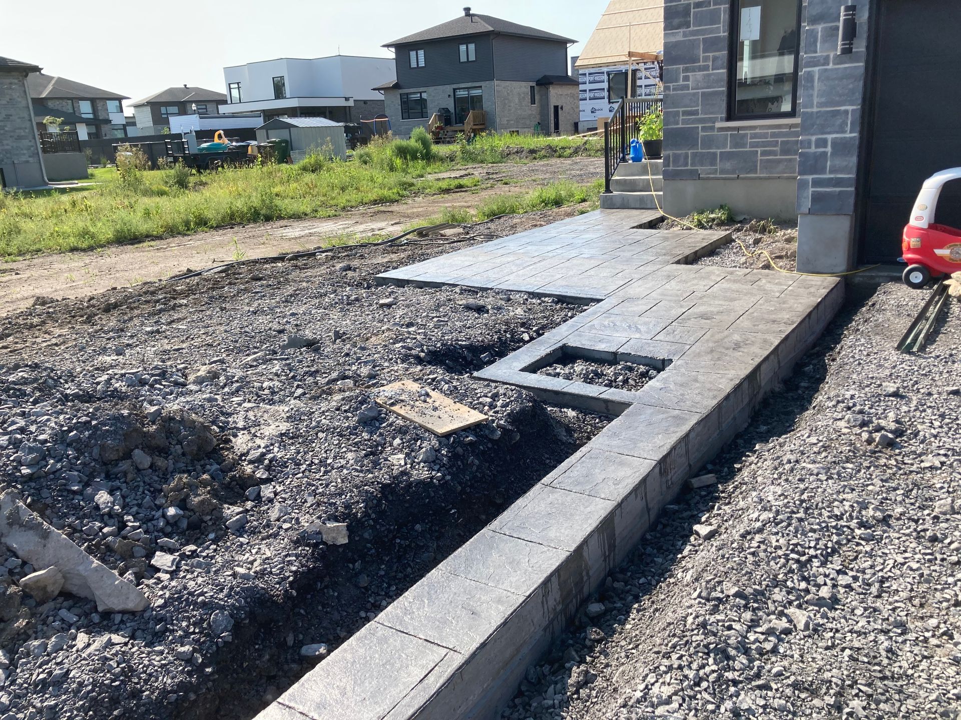 Une petite voiture rouge est garée devant une maison en construction.