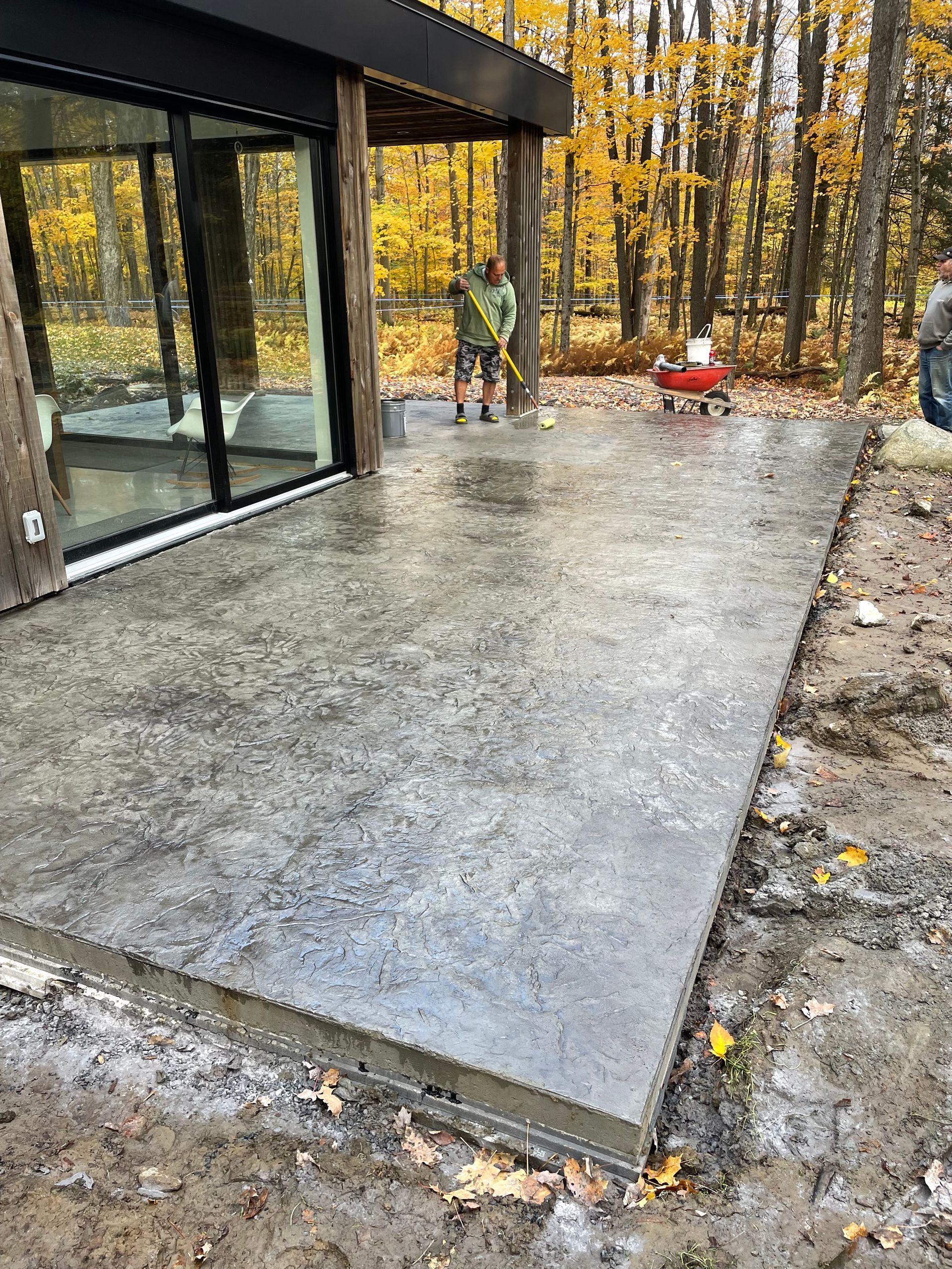 Un homme se tient debout sur une terrasse en béton devant une maison.