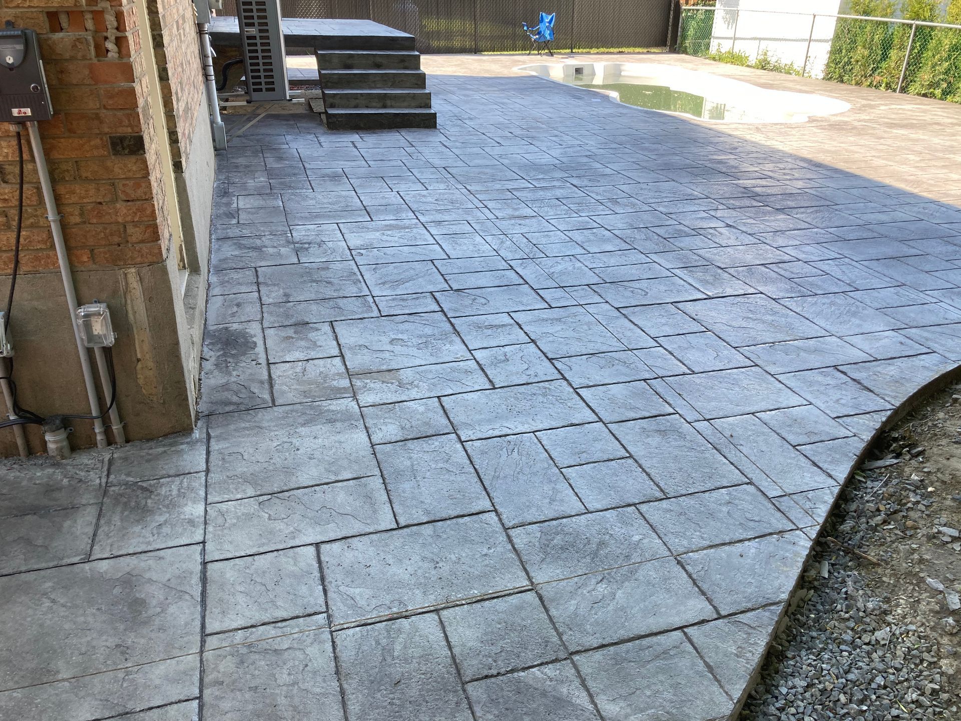 Un patio en béton avec des escaliers et une piscine en arrière-plan.