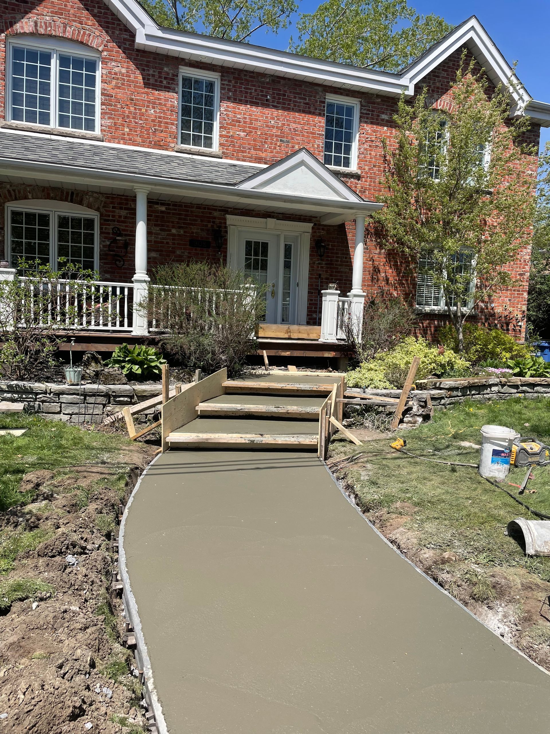 Une passerelle en béton est en cours de construction devant une maison en briques.