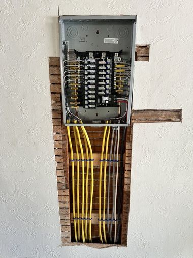 Electrical panel installed in a wall opening, with yellow and grey electrical cables visible.