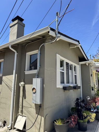 Lineman in a lift truck working on power lines, wearing a hard hat, in a residential neighborhood.