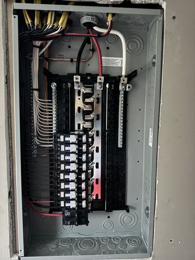 Electrician in yellow hard hat working on wiring inside a wall.