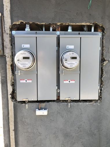 Electrician in yellow hard hat working on wiring inside a wall.