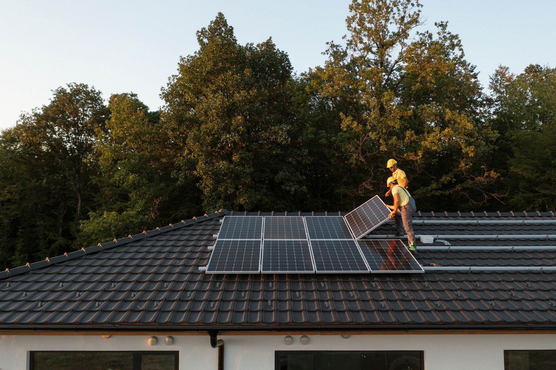 Solar panel installer on rooftop placing panels. Trees in background.