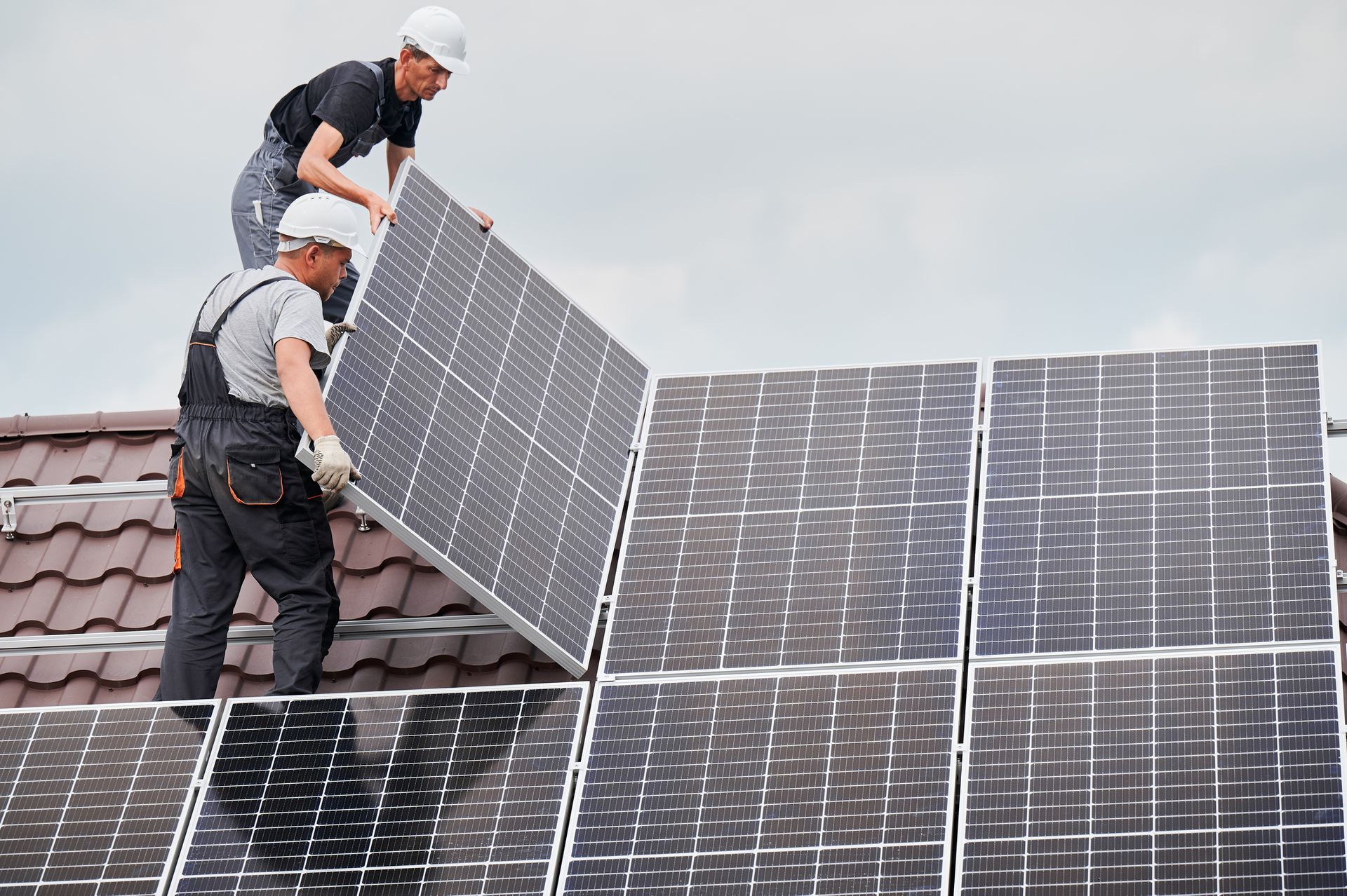 Two workers in hard hats installing solar panels on a roof.