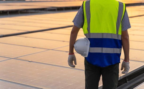 Construction worker wearing a reflective vest and gloves, holding a hard hat on a rooftop.