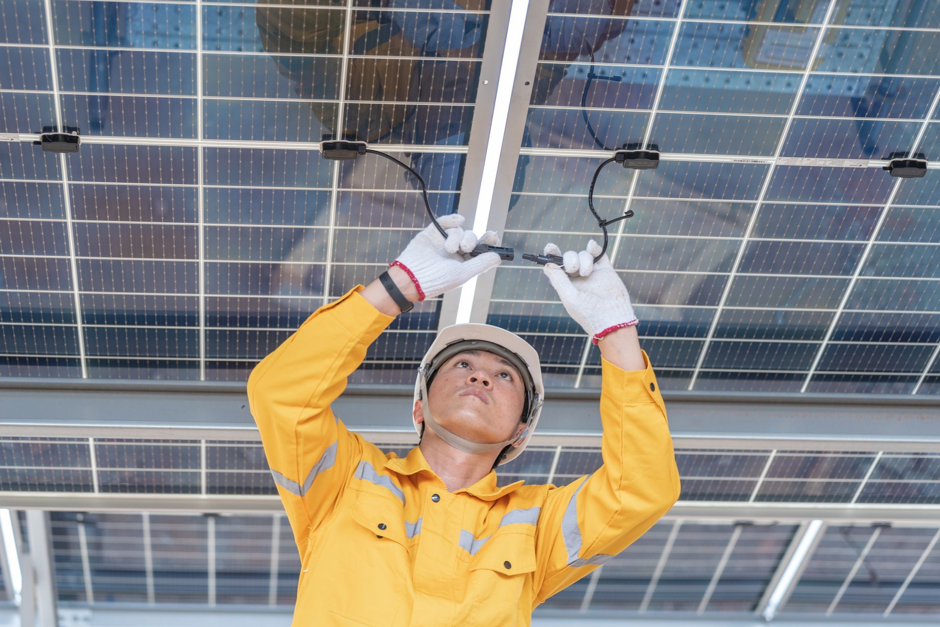 Construction worker in a yellow uniform installing wires on solar panels.