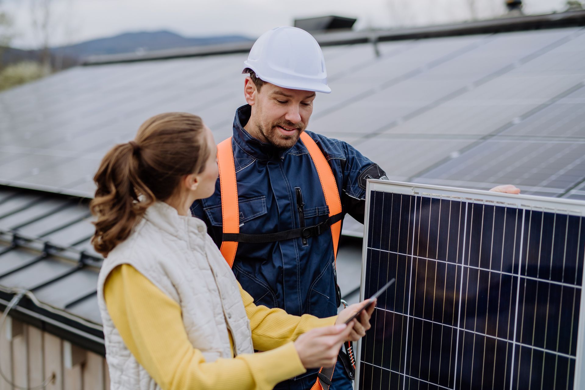 Woman and worker examining solar panel on a rooftop.
