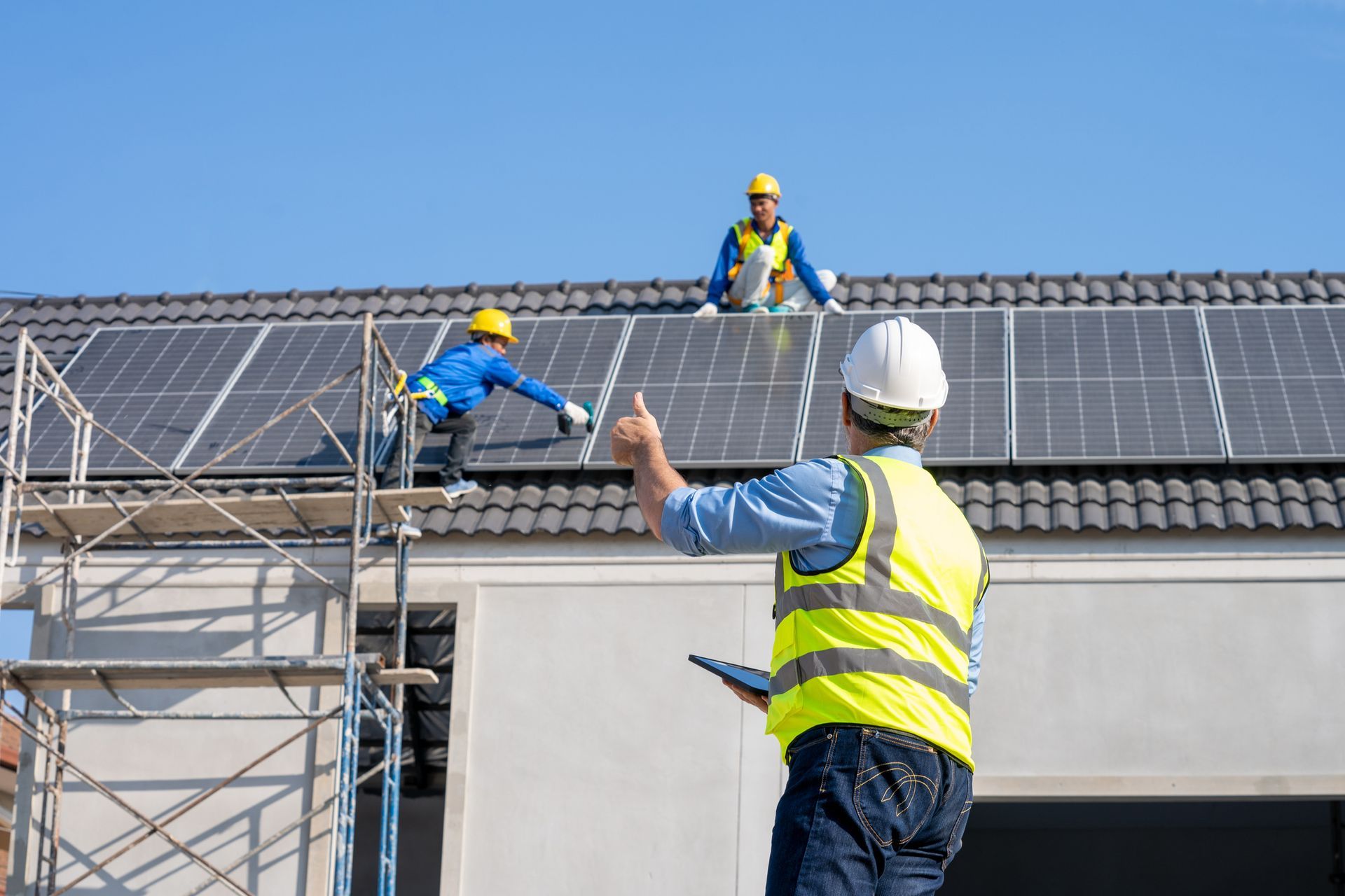 Construction workers installing solar panels on a rooftop. One gives a thumbs up.