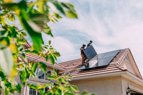 Two workers installing solar panels on a residential roof under a sunny sky.
