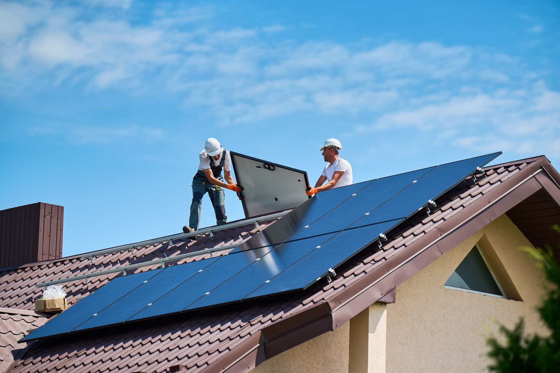Two workers installing solar panels on a roof against a blue sky.