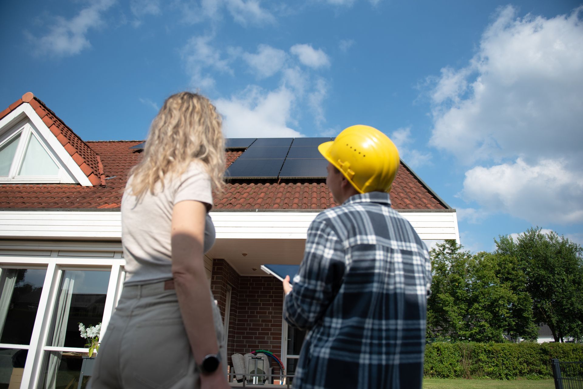 Woman and construction worker examining solar panels on a house roof.
