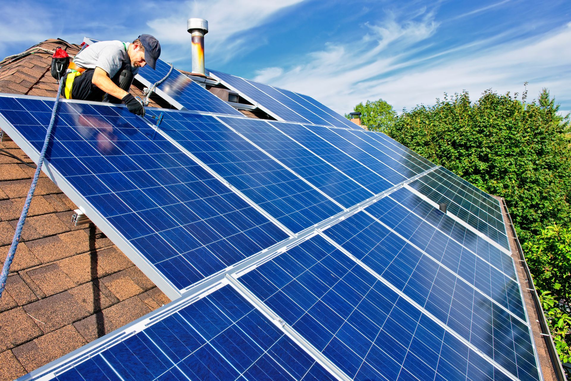 Worker installing solar panels on a brown roof under a blue sky.